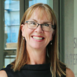 Portrait photo of Jill wearing a black top. She has shoulder length hair and is wearing glasses