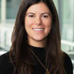 Portrait photo of Henrietta. Henrietta has long dark hair and is wearing a black top and gold necklace