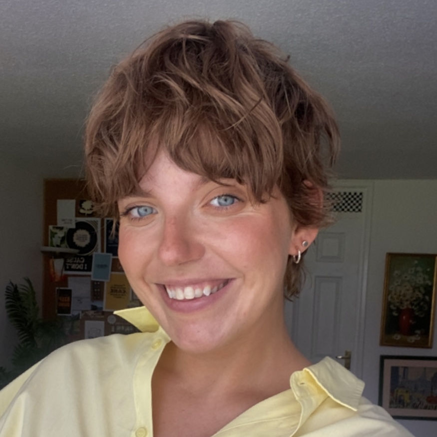 Head and shoulders photo of Jenny, a white woman with short brown hair smiling. She is wearing a yellow shirt.