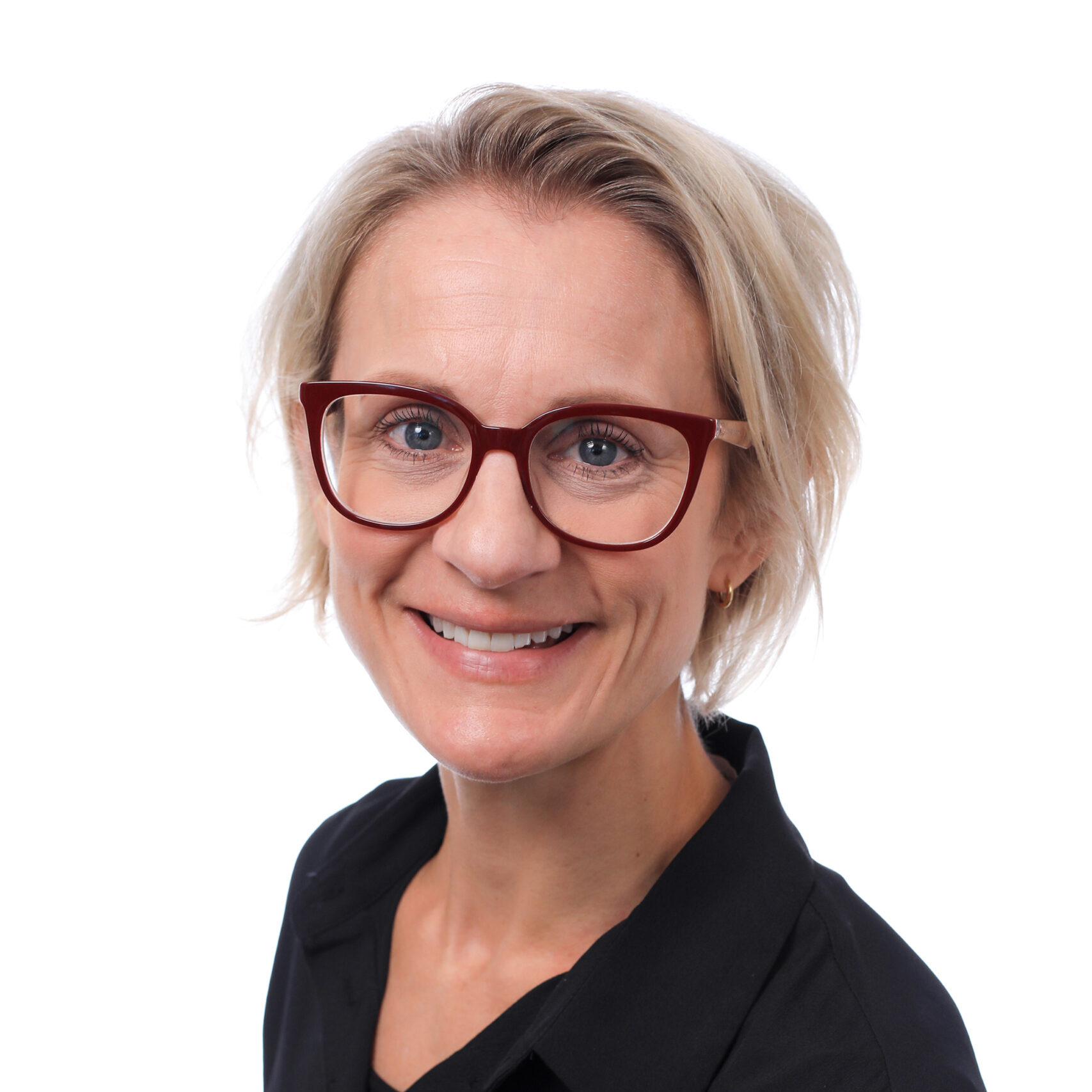 Portrait photo of Charlotte who is smiling. She has short blonde hair and is wearing glasses.