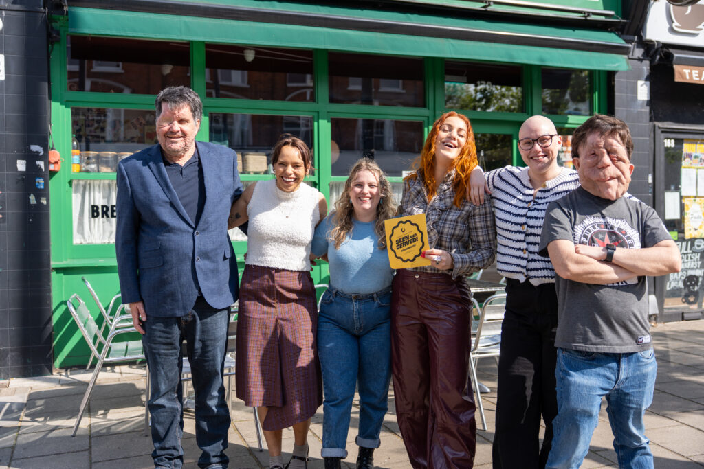 Image shows a range of people with facial differences of varying ages and genders standing individually smiling to camera.