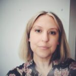 Photo shows Steph facing the camera, they have blonde shoulder length hair and are wearing a patterned dress.